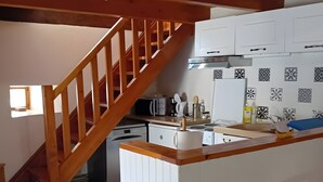 Une cuisine avec des meubles blancs, un escalier en bois et un pare-feu en carreaux.