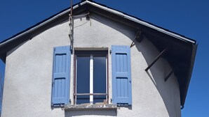 Un bâtiment doté d’un toit à pignon, d’une fenêtre avec des volets bleus et d’une petite porte.