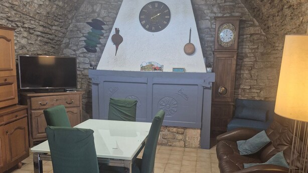 Une pièce chaleureuse avec un plafond en pierre, une table à manger avec des chaises, un canapé, un téléviseur et une horloge.