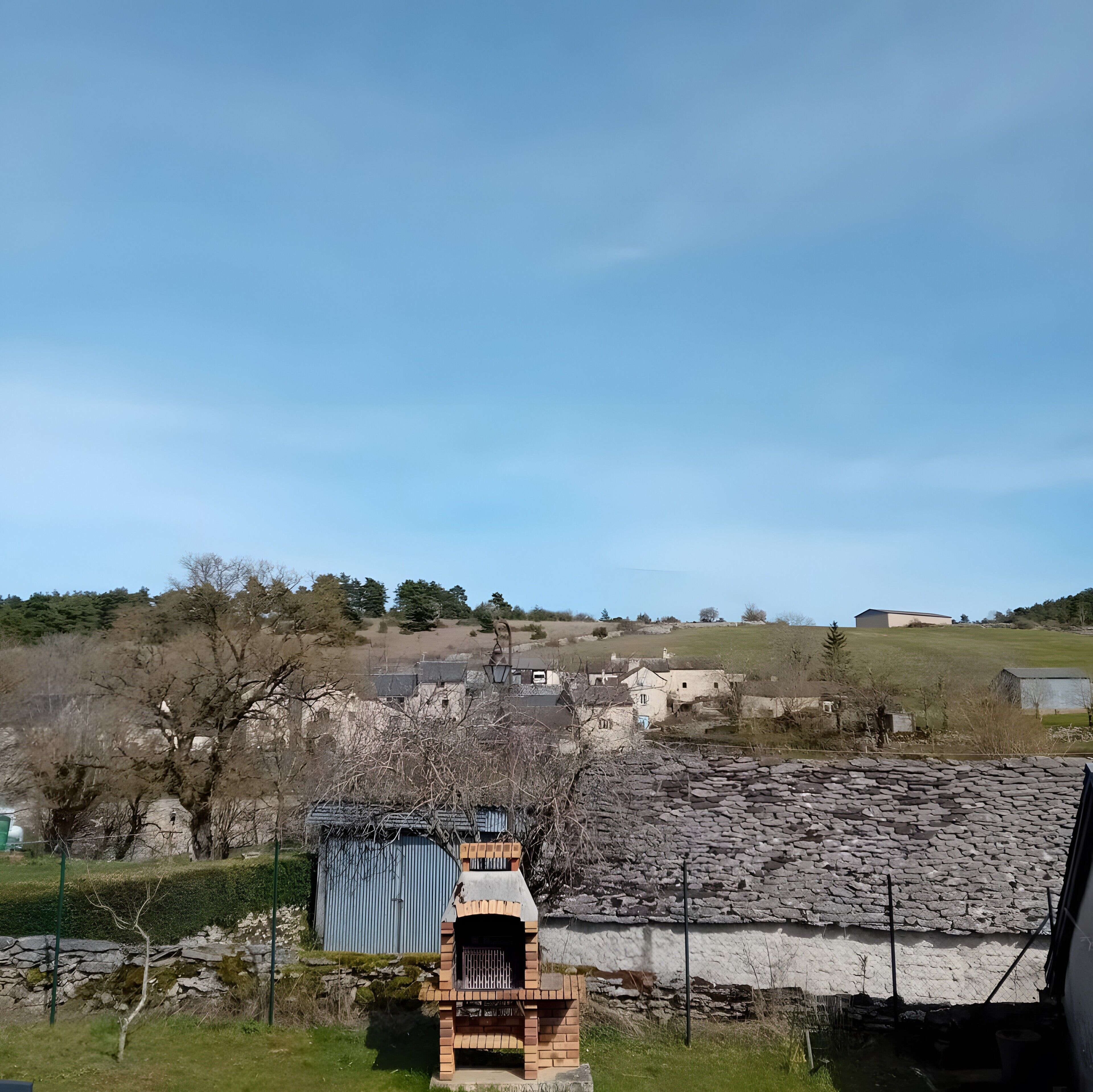 A rural landscape with stone buildings, a brick oven, and a clear sky.