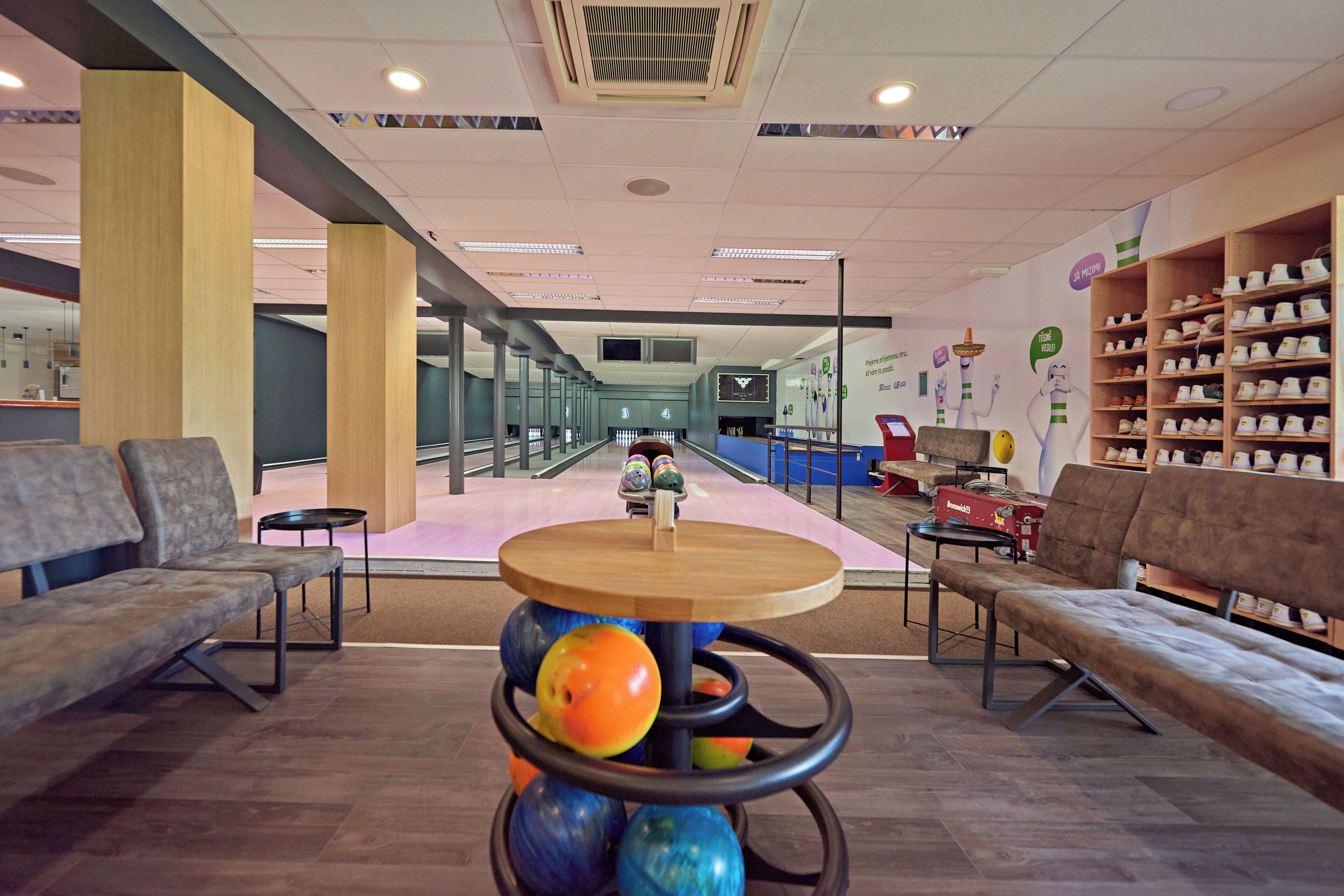 Une salle de bowling avec une table en bois au premier plan, des pistes de bowling en arrière-plan et des étagères remplies de chaussures de bowling sur la droite.