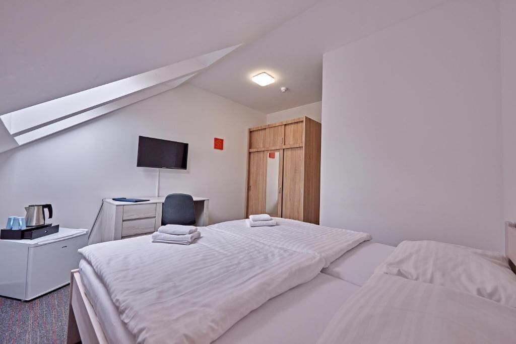 A hotel room with a bed, a desk with a computer, a TV, and a wardrobe.