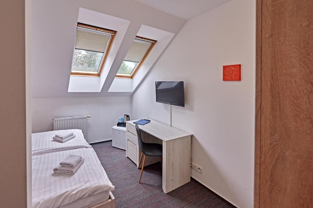 Une chambre avec deux lits, un bureau, une chaise, une télévision et deux fenêtres de toit.