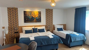 A hotel room with two beds, a desk, and a chair. There are wall art and a ceiling fan.