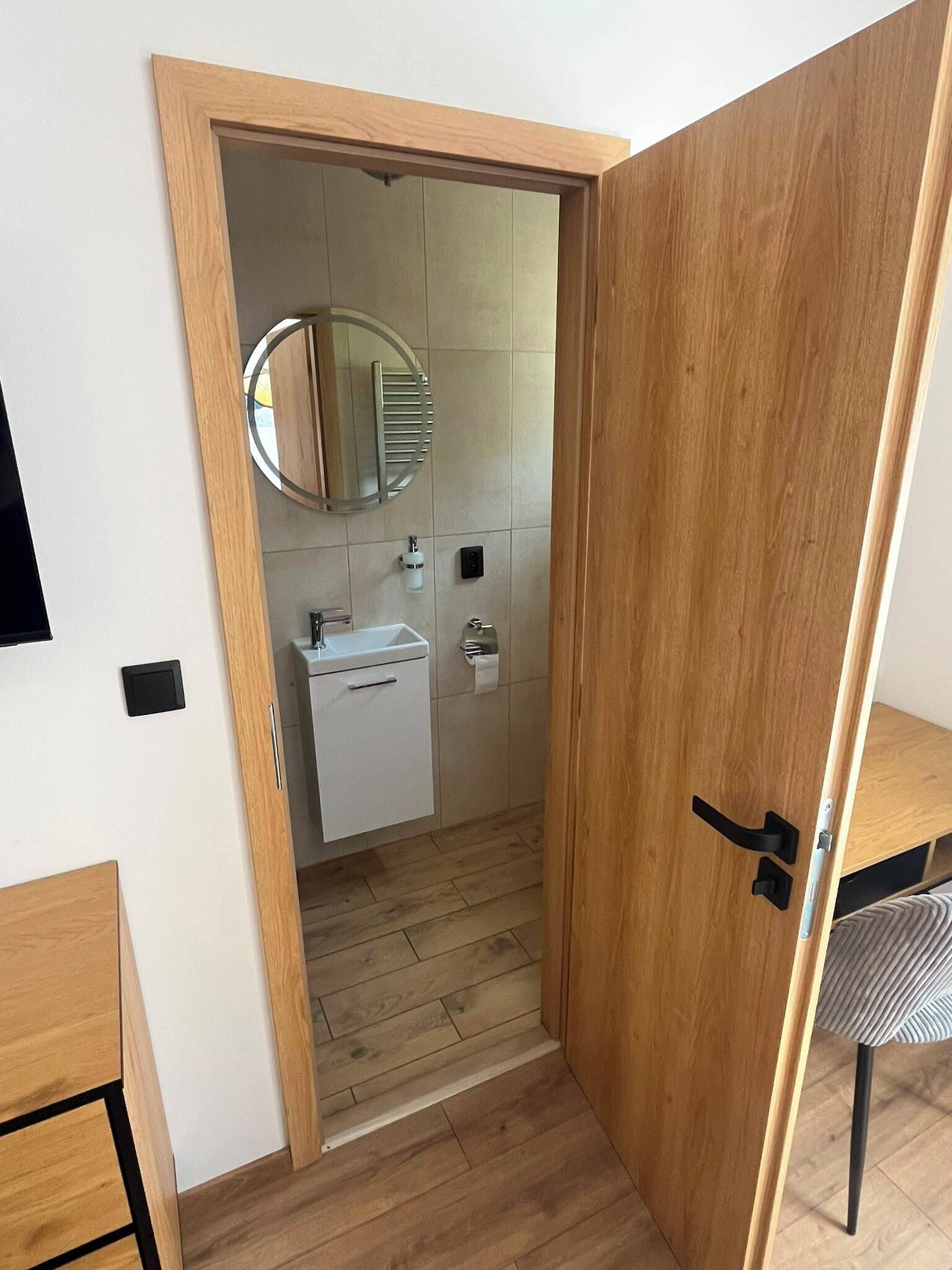 Un baño moderno con puerta de madera, lavamanos, espejo e inodoro.
