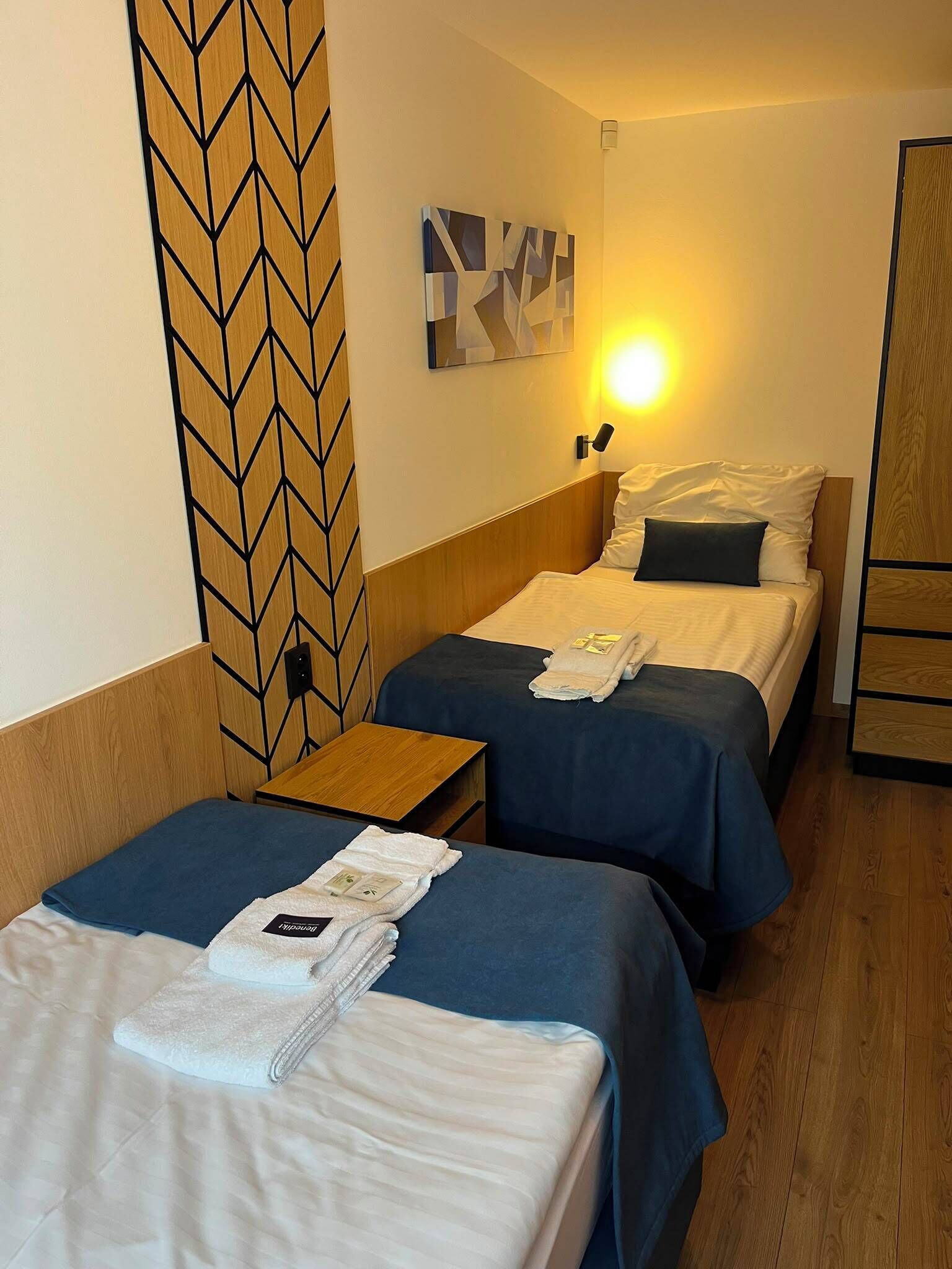Una camera d'albergo con due letti, una testiera in legno, un'opera d'arte appesa al muro e un comodino con una lampada.