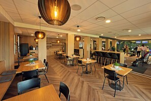 A spacious indoor area with multiple tables and chairs, wooden flooring, and modern pendant lighting. - Benedikt (Most)