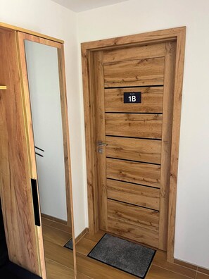 Een houten deur met een nummerplaat waarop kamer 1B staat, een deurklink en een deurmat.