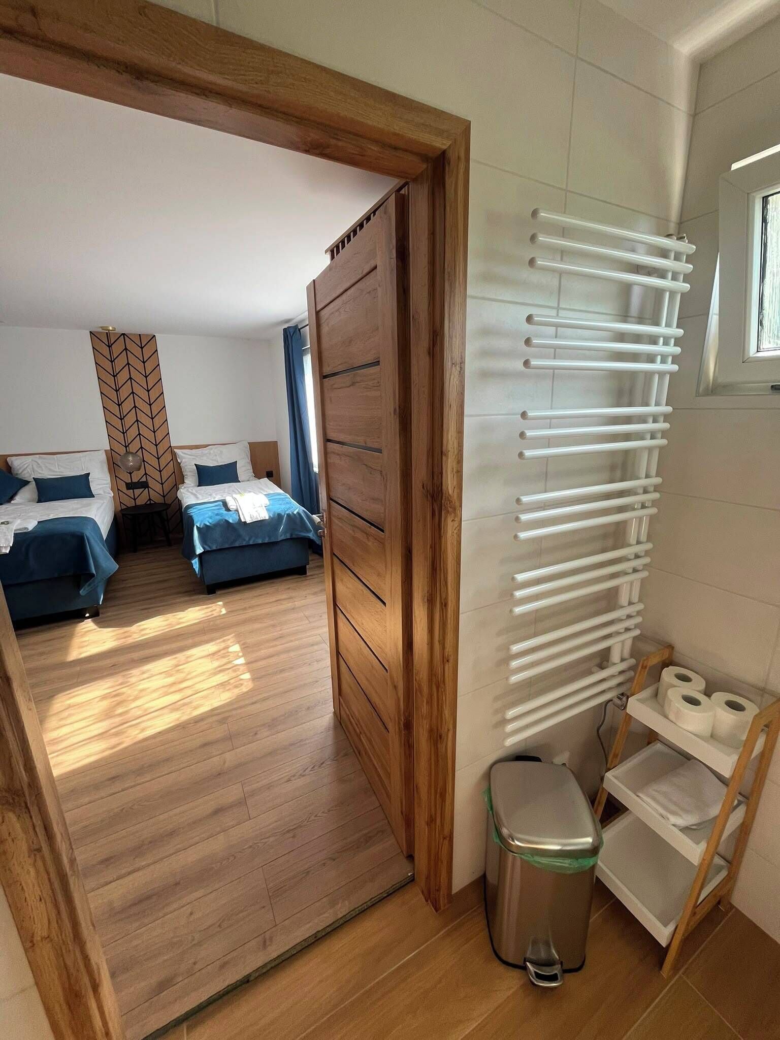 Une chambre d’hôtel avec deux lits, une armoire en bois, un radiateur, une poubelle et une fenêtre.