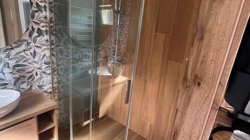 A modern bathroom with a glass shower enclosure, wooden flooring, and a sink with a decorative backsplash.