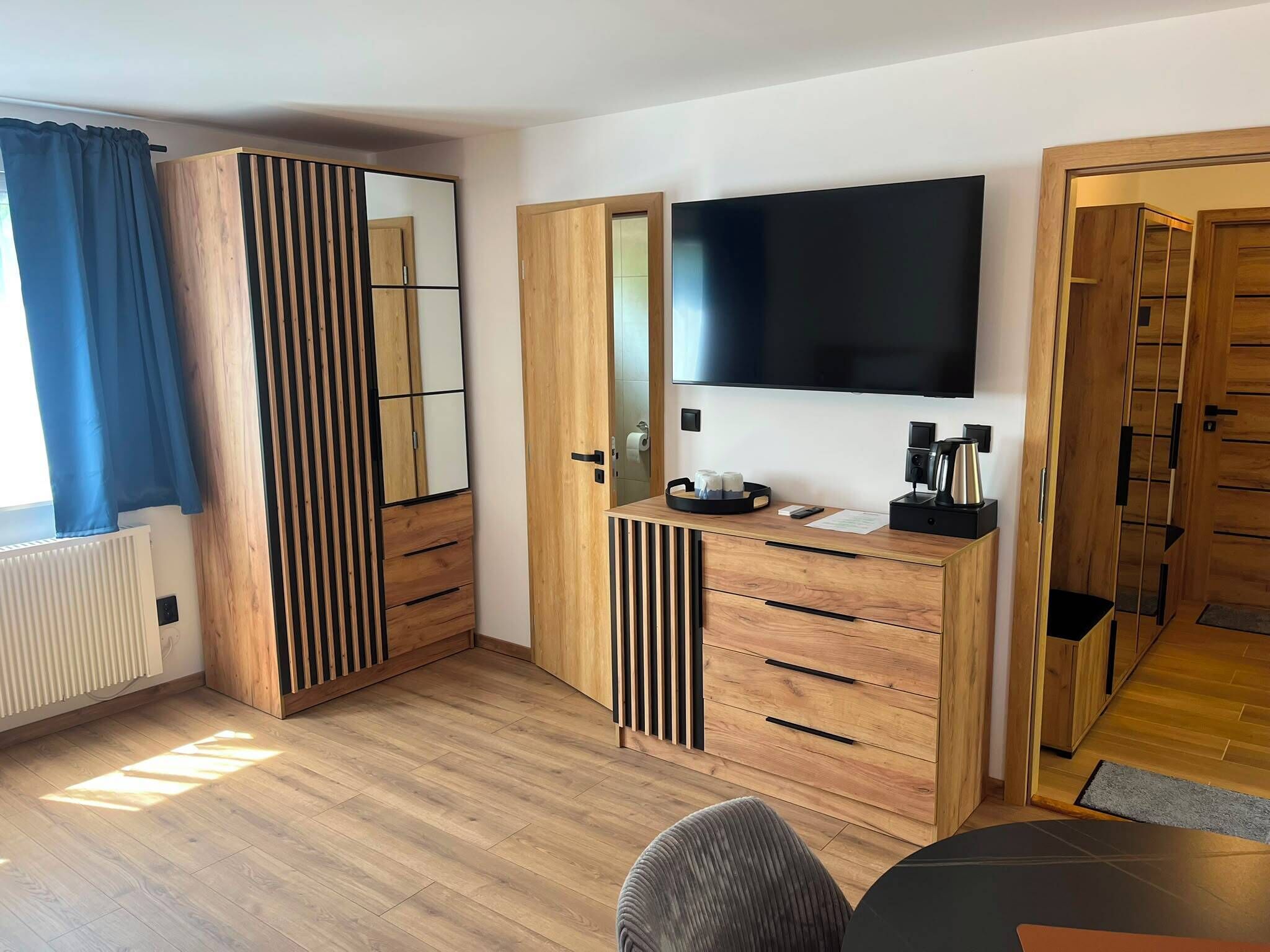 A modern bedroom with a large wardrobe, a TV, and a desk with a kettle.