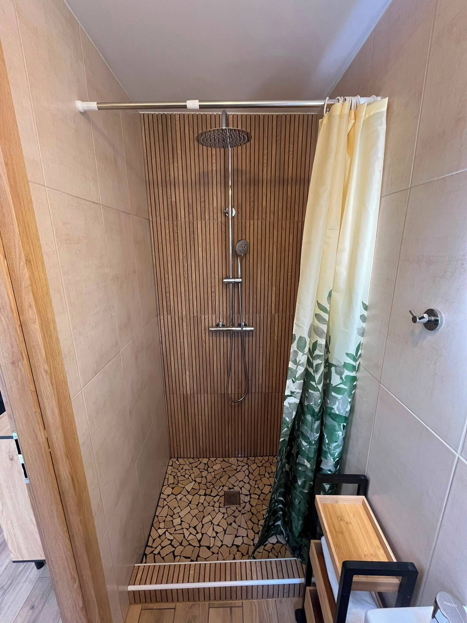 Une douche avec un mur en panneaux de bois, un sol carrelé et un rideau orné d’un motif de feuilles.