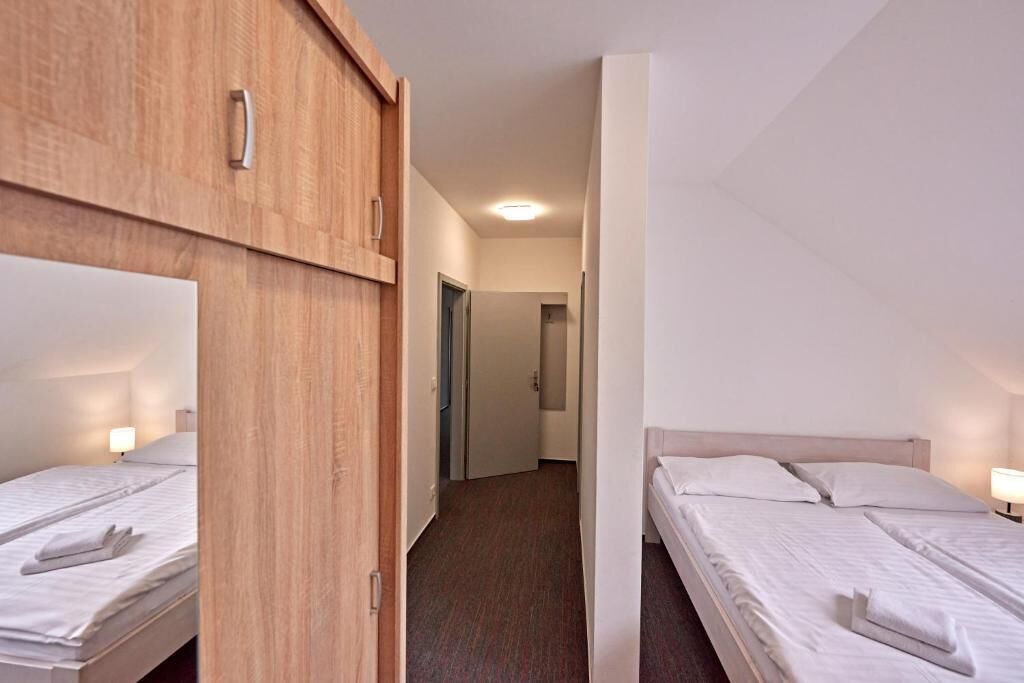 Habitación de hotel con un armario de madera, una cama con sábanas blancas y un pasillo que conduce a otra habitación.