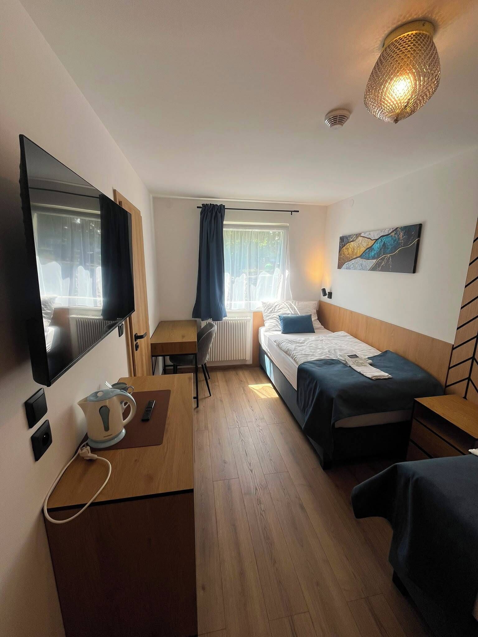 Una habitación de hotel con cama, escritorio con hervidor, televisor y ventana con cortinas.