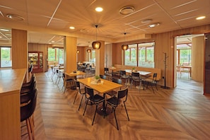 Un vaste espace dédié à la salle à manger, avec de nombreuses tables et chaises, un plancher en bois et de grandes fenêtres qui laissent entrer la lumière naturelle.
