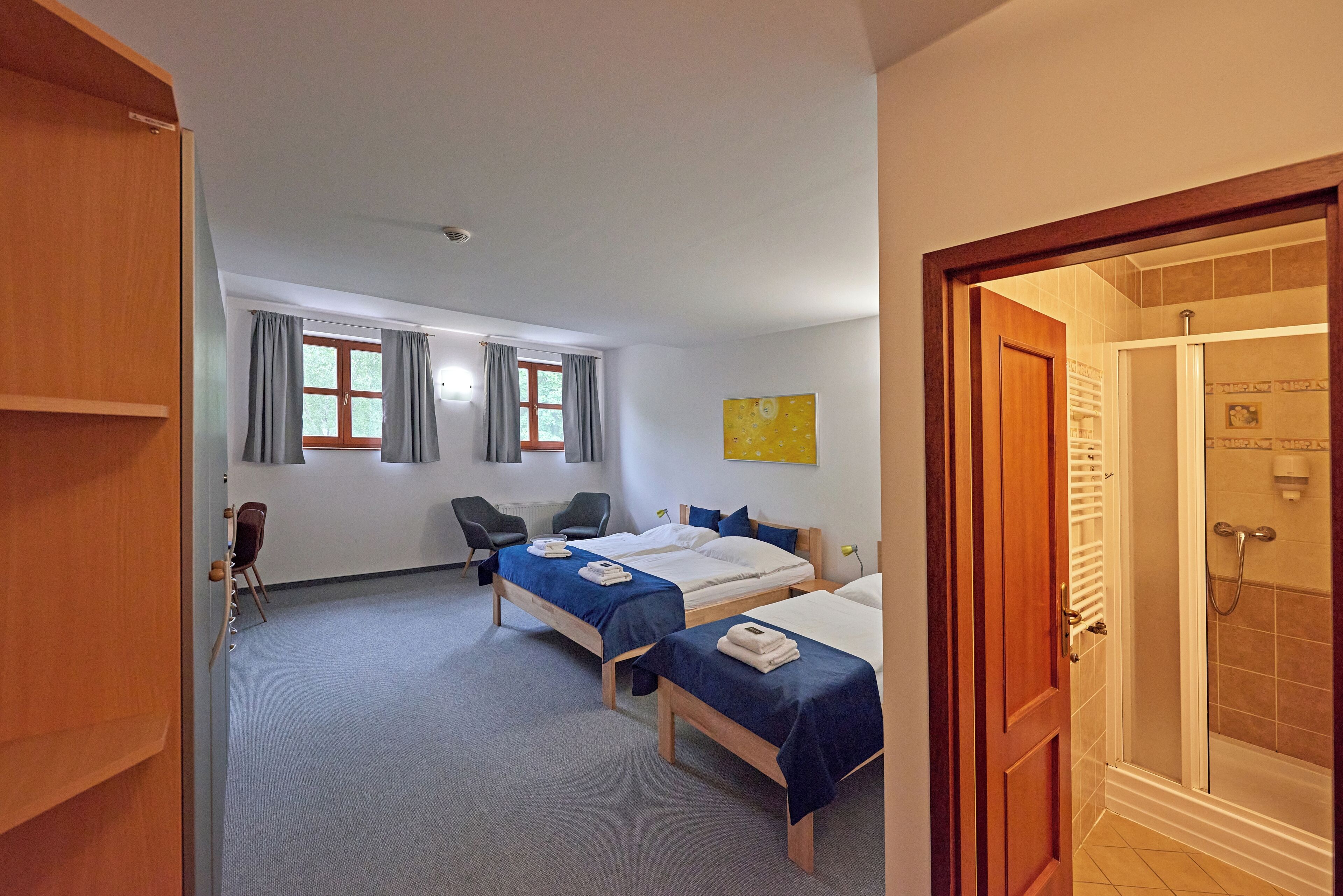 A hotel room with two beds, a desk, a chair, and a shower area.
