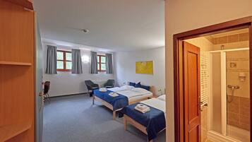 A hotel room with two beds, a desk, a chair, and a shower area.