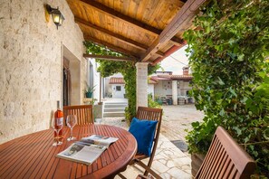 An outdoor patio with a wooden table and chairs, a wine glass, and a magazine. - Villa STOCK 66 - Charming villa with private pool (Stokovci)