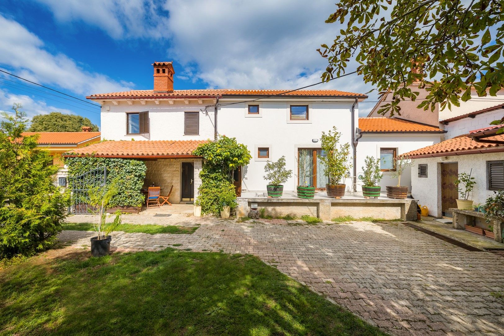 A two-story house with a tiled roof, a paved courtyard, and potted plants.