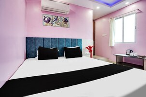A hotel room with a bed, a desk, a window, and an air conditioning unit.