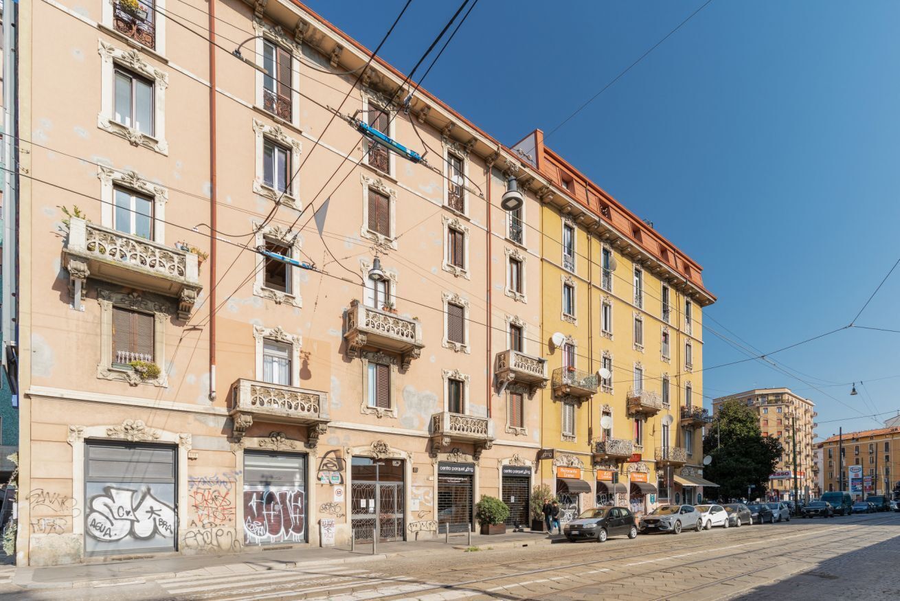 A multi-story building with balconies, storefronts, and parked cars.