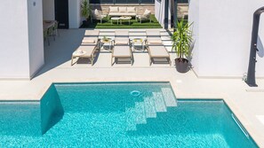 A swimming pool with lounge chairs and a small table, surrounded by a white wall and a grassy area with a sofa and chairs. - NEW! Discover Villa Logos: Your Seaview Retreat in Croatia (Dugi Rat)