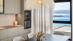 Een moderne keuken met een eethoek, een groot raam met uitzicht op zee, en een decoratieve lamp.