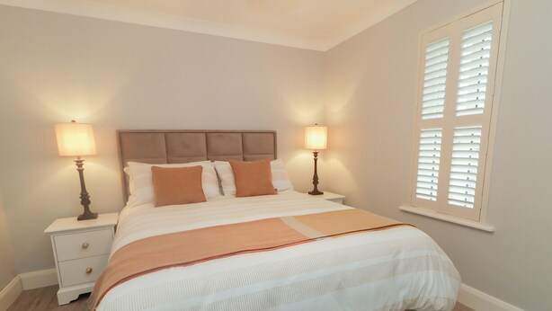 A bedroom with a bed, two bedside tables, a nightstand, a window with blinds, and a wooden floor. - Portnablagh Cottage (Portnablagh)