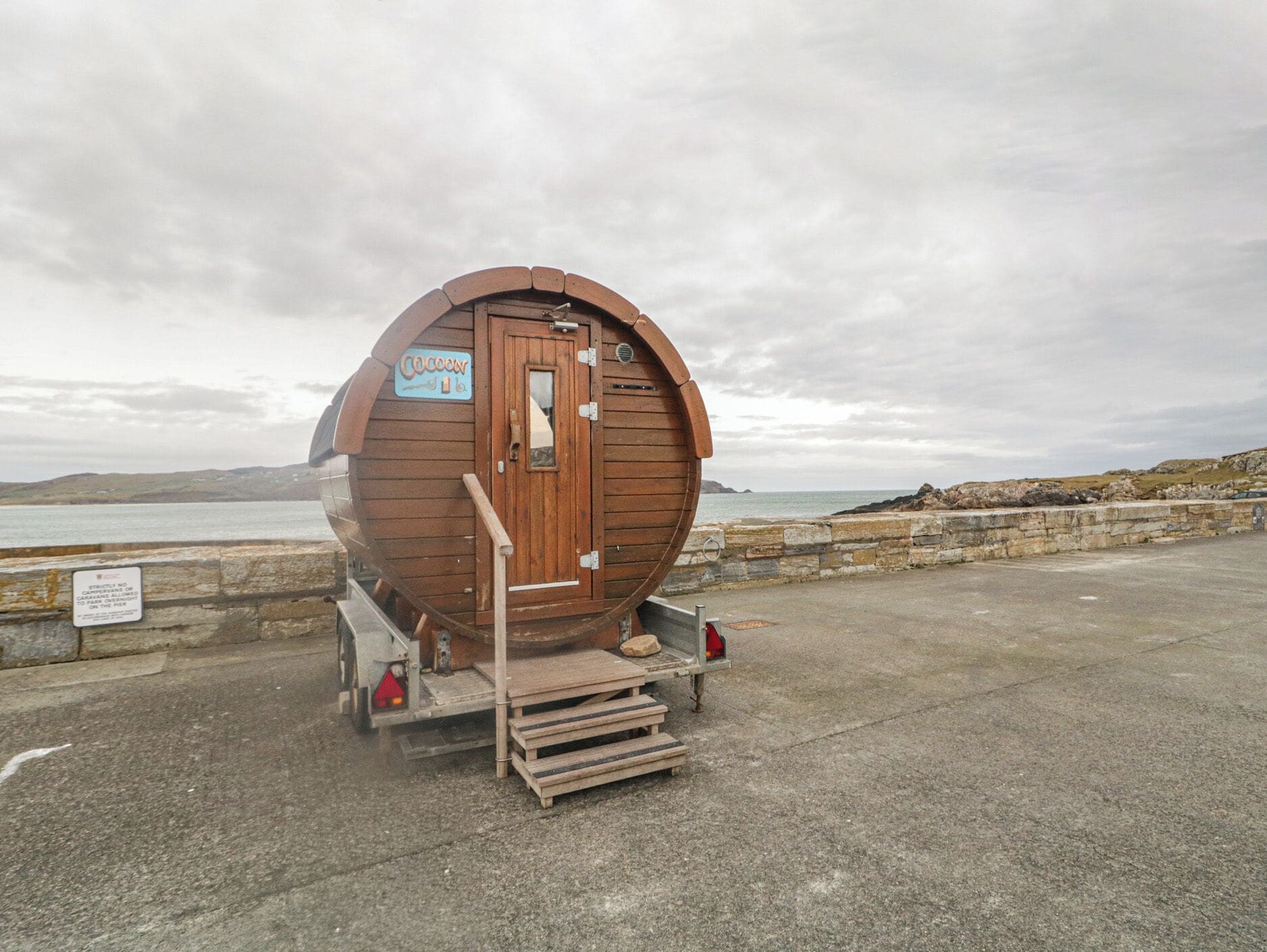 Un edificio con forma de barril de madera, una puerta, un letrero y una rampa que lleva a un vehículo.