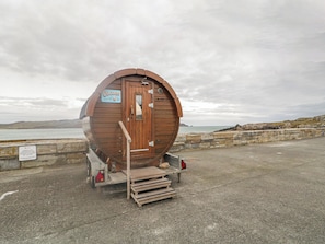 A wooden barrel-shaped building with a door, a sign, and a ramp leading to a vehicle. - Portnablagh Cottage (Portnablagh)