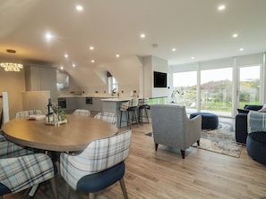 A modern kitchen with a dining area, a bar, and a large window offering a view. - Portnablagh Cottage (Portnablagh)