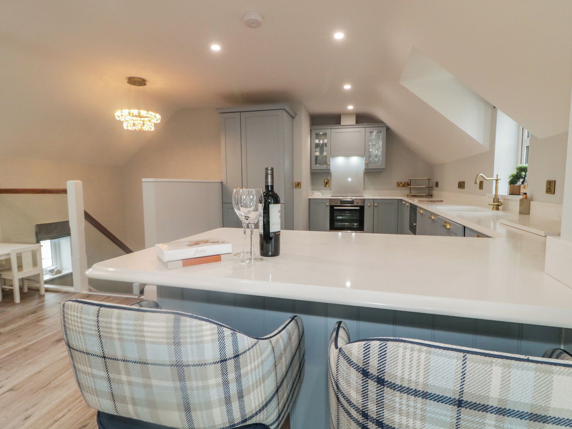 A modern kitchen with a central island, a dining area with two chairs, and a staircase leading to an upper level.