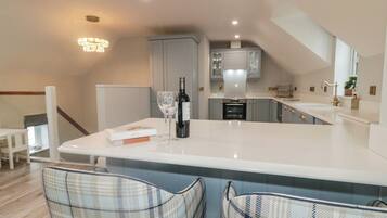 A modern kitchen with a central island, a dining area with two chairs, and a staircase leading to an upper level.