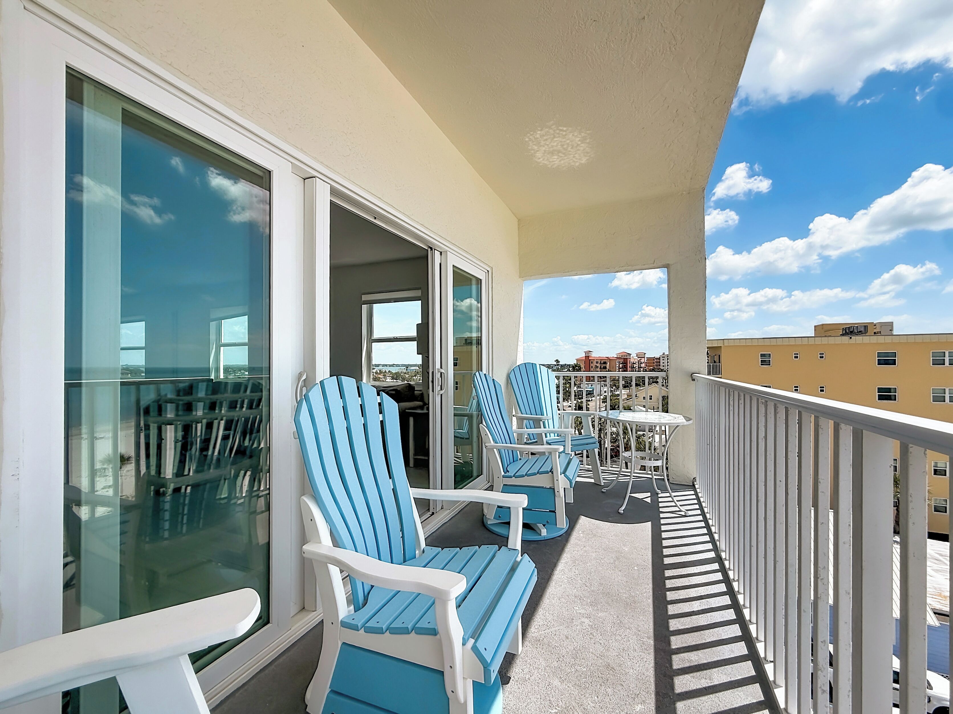 A balcony with two blue Adirondack chairs, a small round table, and a glass door leading to an indoor area.