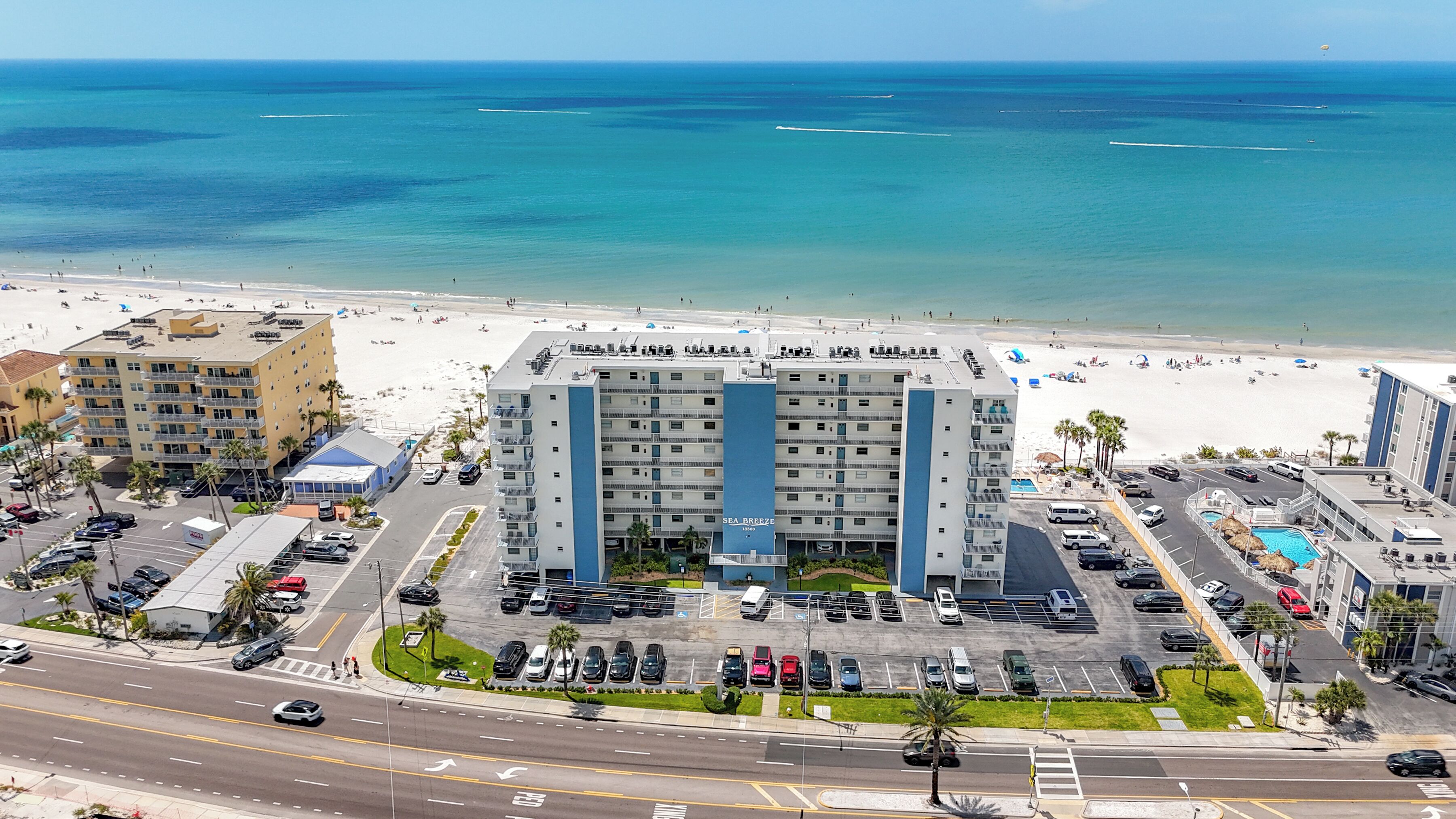 A hotel with a parking lot, a pool, and a view of the beach and ocean.