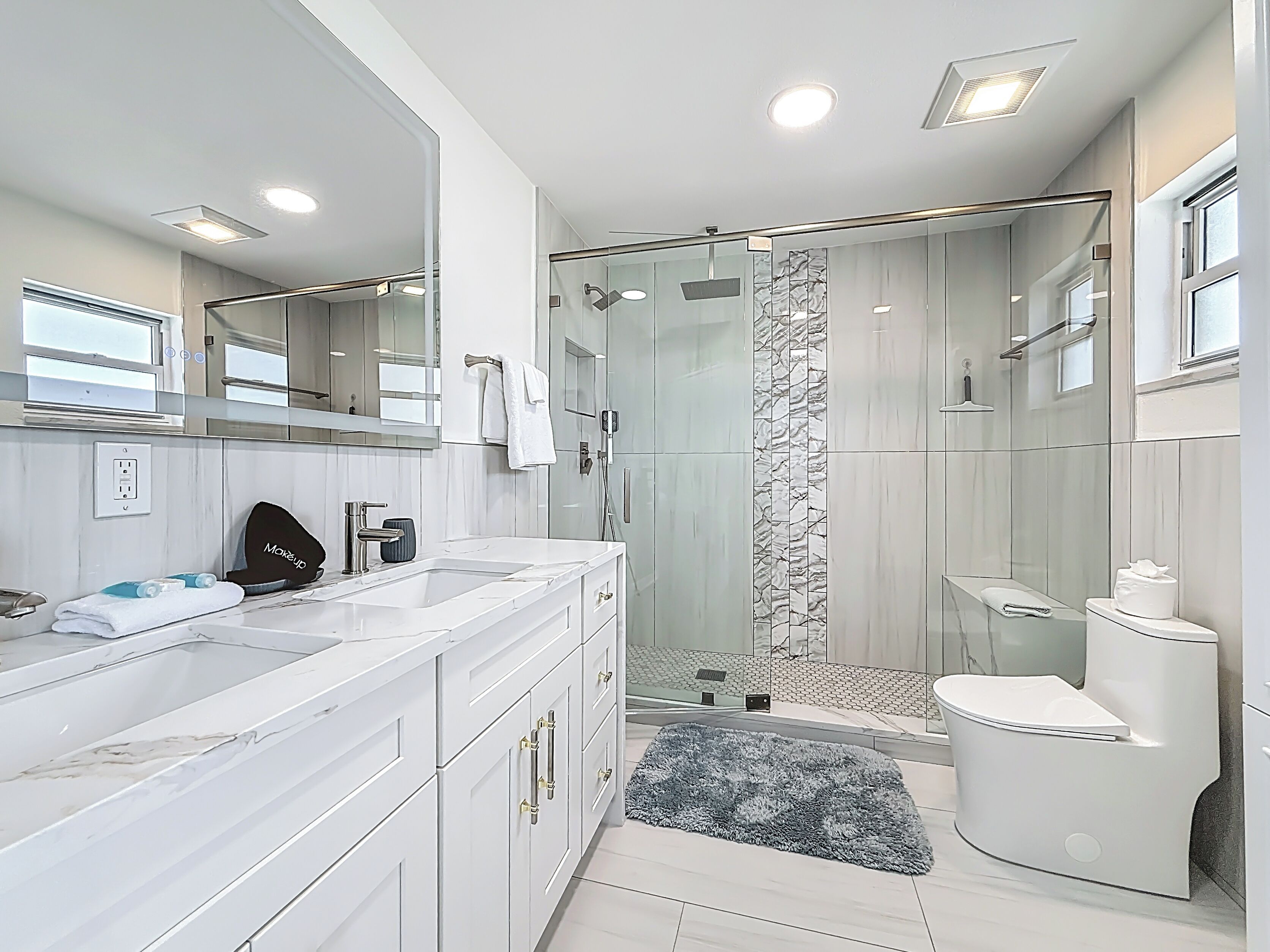 Une salle de bain moderne avec une douche à parois de verre, des toilettes blanches et un meuble-lavabo en marbre.