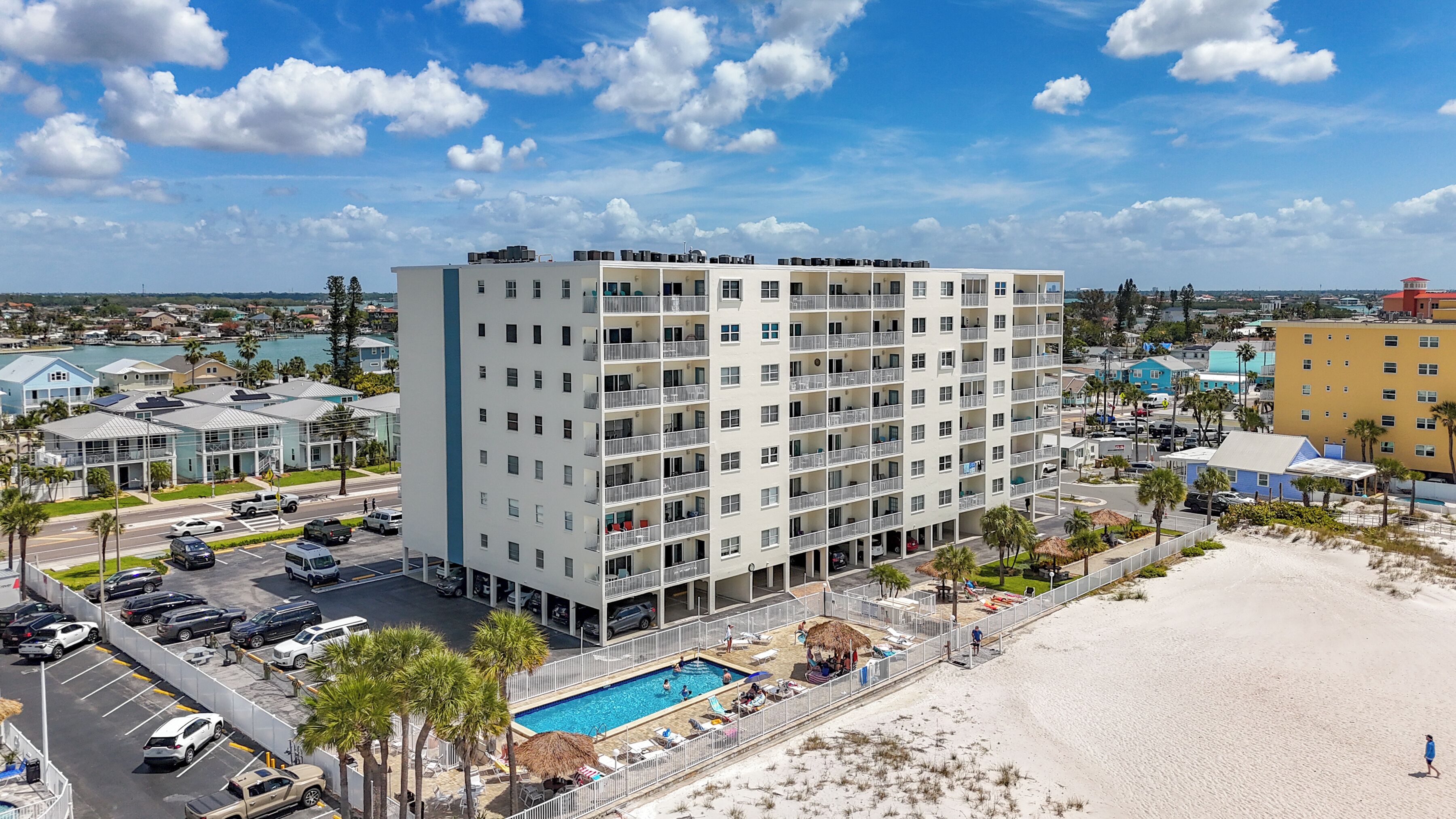 A multi-story hotel with a swimming pool, parking, and a beach view.