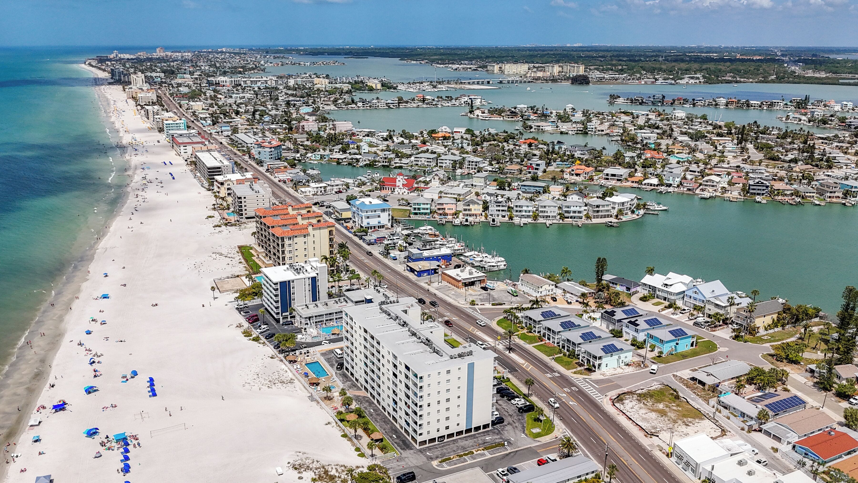 An aerial view of a coastal city with a beach, marina, and residential buildings.