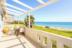 Uma varanda com vista para a praia, uma mesa com cadeiras e um vaso grande.