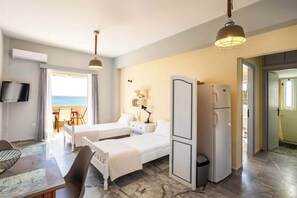 Quarto de hotel com duas camas, televisão, frigorífico, mesa e cadeiras, e vista para o mar.