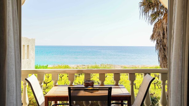 En balkon med et bord og stole, der giver udsigt over en strand og havet.