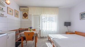 Hotellihuone, jossa on sänky, työpöytä tuolilla, pieni pöytä maljakolla, televisio yöpöydällä ja ikkuna, jossa on verhot.
