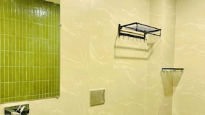 Une salle de bain avec un lavabo noir, un miroir, une douche dont le sol est recouvert de carreaux verts et un bac de rangement noir.