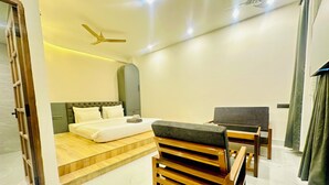 Une chambre d’hôtel moderne équipée d’un lit, d’un bureau, d’une chaise, d’un ventilateur de plafond et d’une grande fenêtre avec des rideaux.