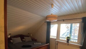 Ein Schlafzimmer mit einem hölzernen Bett, einer Pendelleuchte, einem Fenster mit Ausblick und einer Heizung.