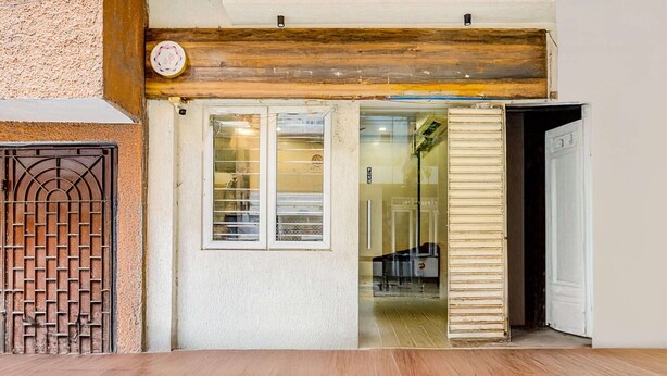 Entrada de hotel con piso de madera, una reja metálica y un puerta de vidrio que da al interior.