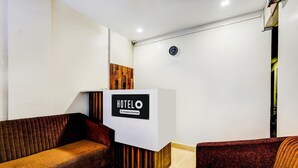 Un mostrador de recepción de hotel con un cartel, un panel decorativo de madera y dos sofás.