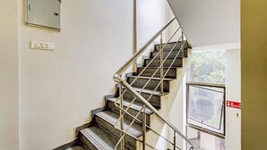 Una escalera con barandillas metálicas, un interruptor de luz en la pared y un ventanal con letrero de salida.