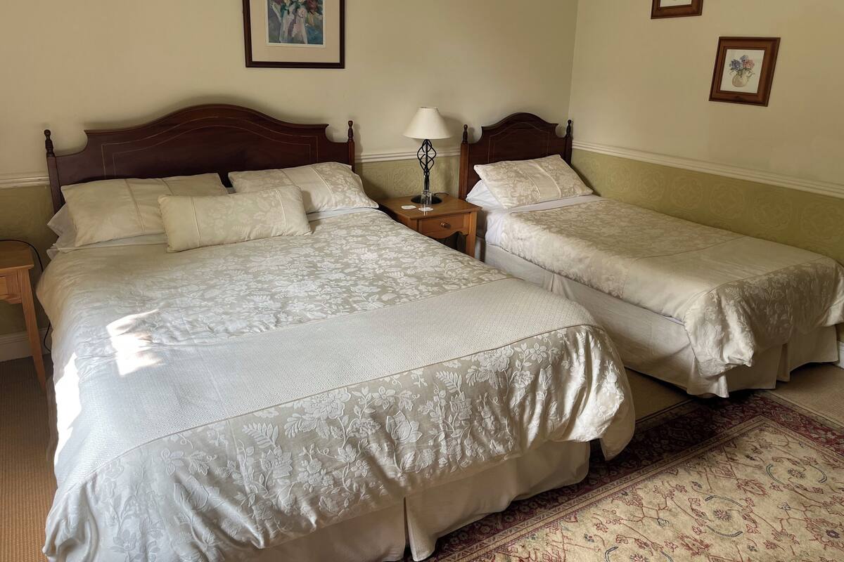 A double bed with a floral bedspread, a nightstand with a lamp, and two framed floral pictures on the wall.