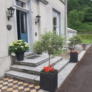 A building with a blue door, white walls, and black lanterns. There are steps leading to the entrance, and potted plants with flowers.